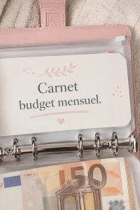 Femme écrivant dans un carnet de budget coloré pour organiser ses finances, avec des fournitures de bureau à proximité.